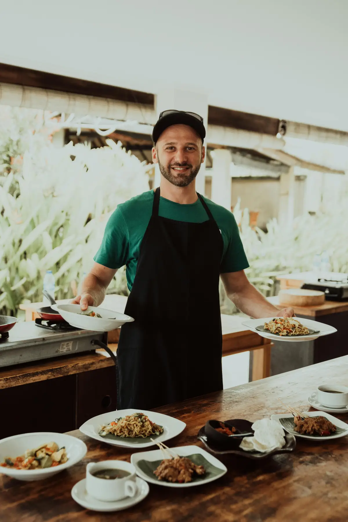 Chef in an open-air kitchen with plates of fresh food on a wooden counter